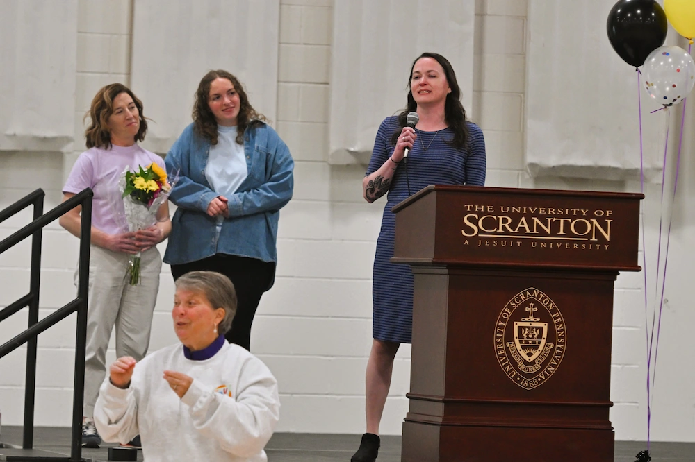 Kim Scatton, mother of Lucas, a 2025 car recipient, shares their story at the 2026 Go Baby Go Community Day. Shown at left are Kaitlyn Gelman ’25, G’26, and Stephanie DeNaples, OTD ’15, G’17. At bottom is Maryanne Stefko, interpreting via American Sign Language.