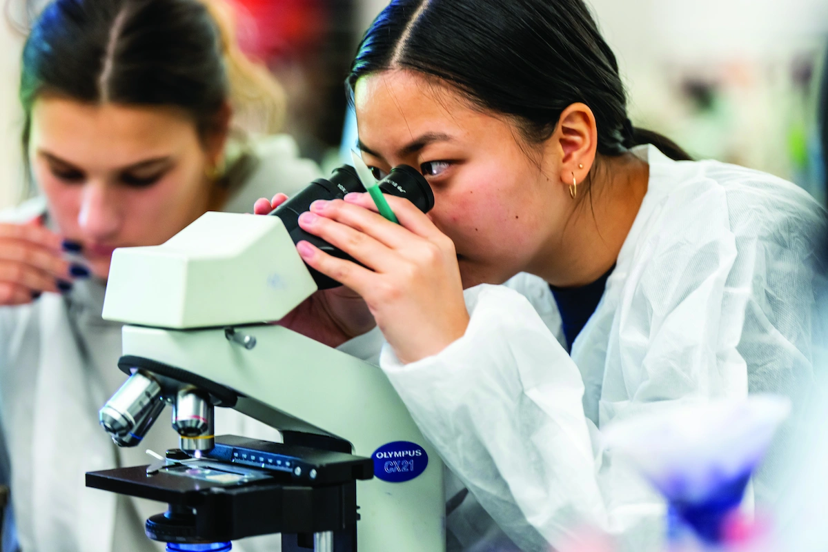 student in lab coat looking through microscope