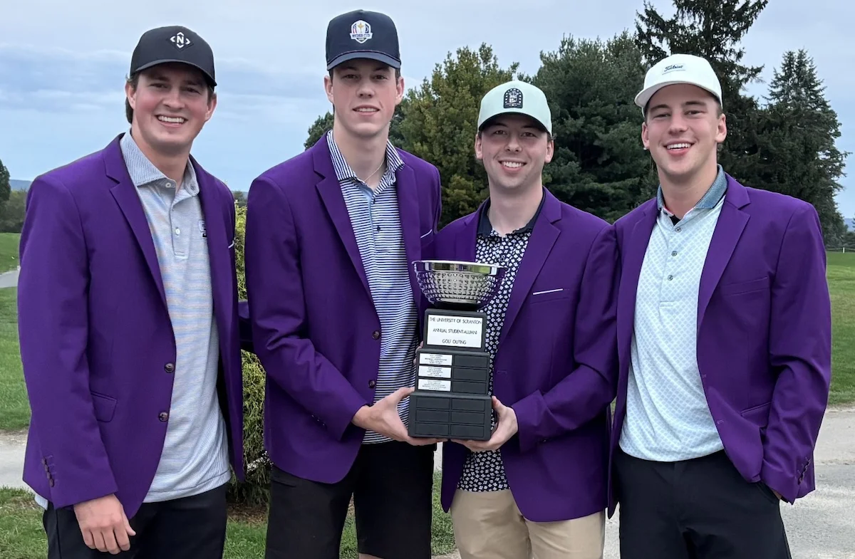 four young golfers wearing matching jackets holding the winning trophy